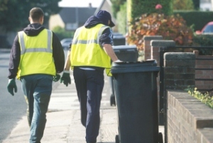 Two workers pulling a green bin