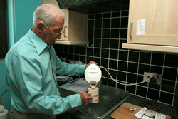 Elderly man pours water from kettle into a mug in a kitchen