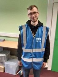 Corey, a young man, wearing overalls and glasses smiling